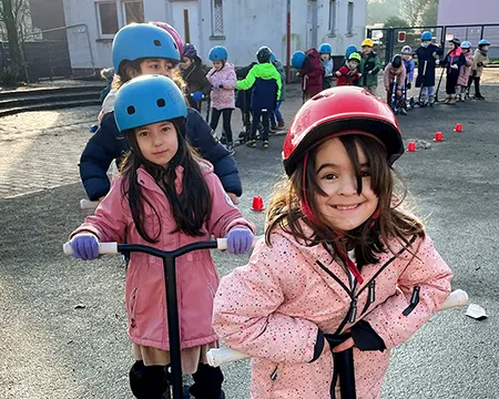 Schülerinnen stehen auf dem Schulhof in einer Schlange mit ihren Rollern und warten auf den Start.
